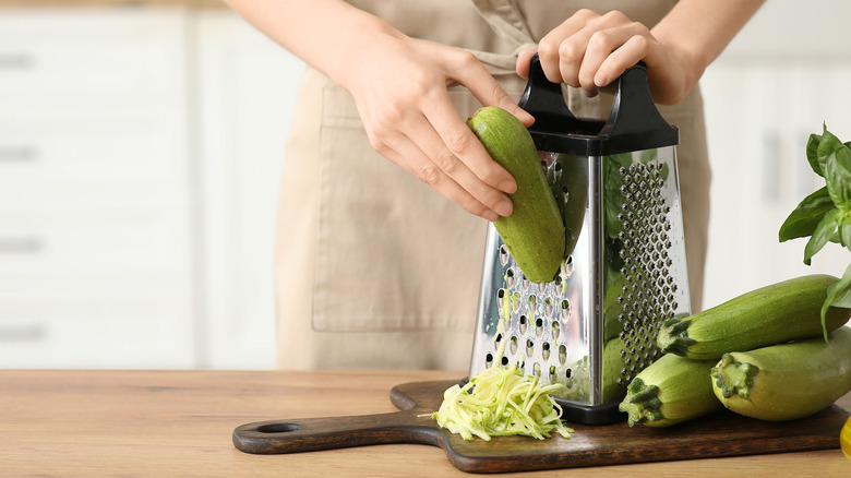 hands grating zucchini on box grater