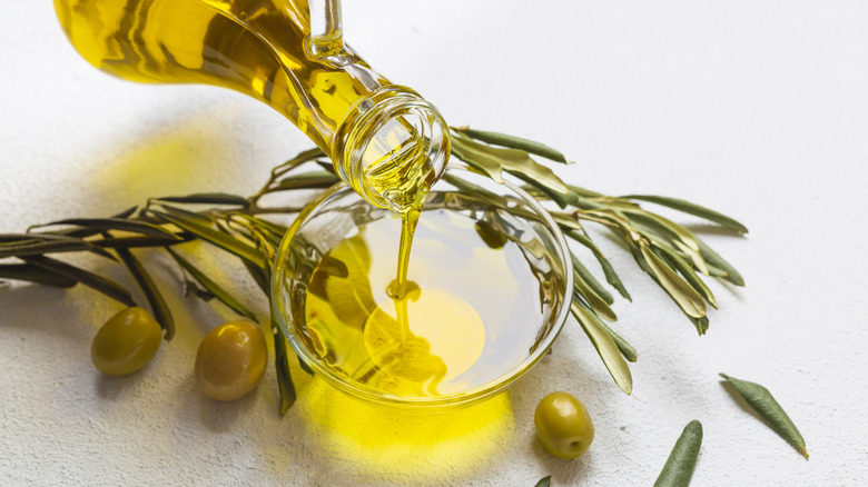 olive oil pouring from jug to bowl with olives and rosemary