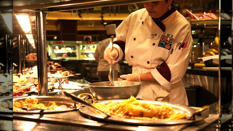 A chef stirs a pot of food behind the counter of a huge buffet platter