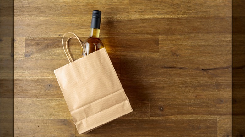 a bottle of white wine is peaking out of a brown paper bag on a wooden tabletop