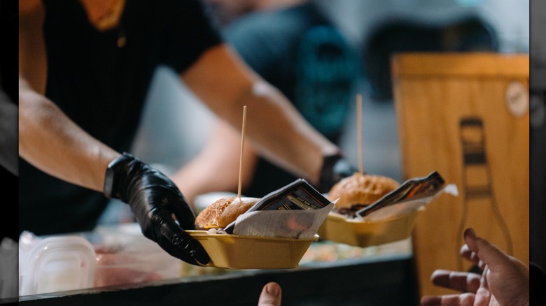 food truck worker hands customer two burgers in open containers