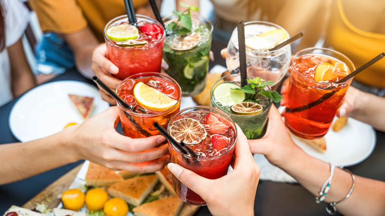 Group of people clinking their cocktail glasses over a spread of snacks