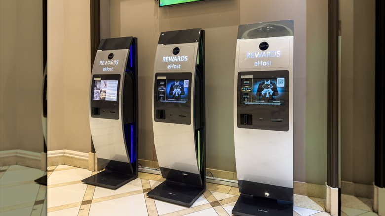 three casino rewards kiosks with touch screens stand against a wall