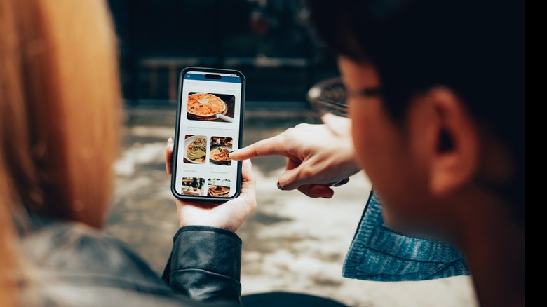 Two people are going through images of food on an iphone