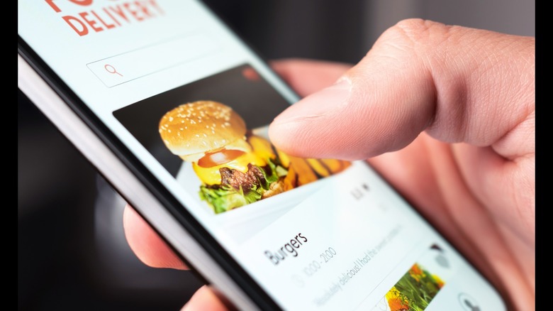 close up of someone on their smart phone, scrolling through a food delivery app showing a burger and fries