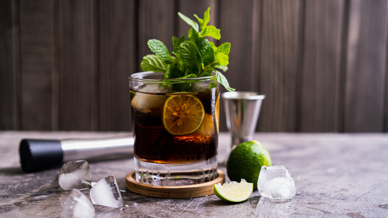 Cola mojito with fresh mint and lime surrounded by bartending tools