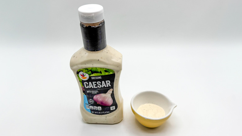 Bottle of Caesar dressing with sample cup of dressing