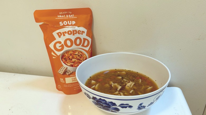 A pouch of Proper Good Chicken Noodle Soup next to a prepared bowl of soup