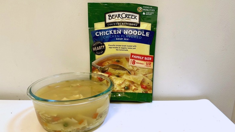 A pouch of Bear Creek Chicken Noodle soup mix next to a prepared bowl of soup