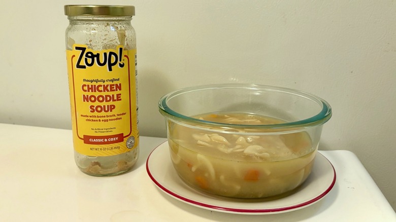 A jar of Zoup! Chicken Noodle Soup next to a bowl of prepared soup