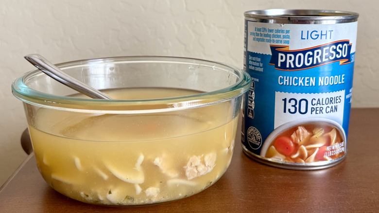 A can of Progresso Light Chicken Noodle Soup next to a bowl of prepared soup