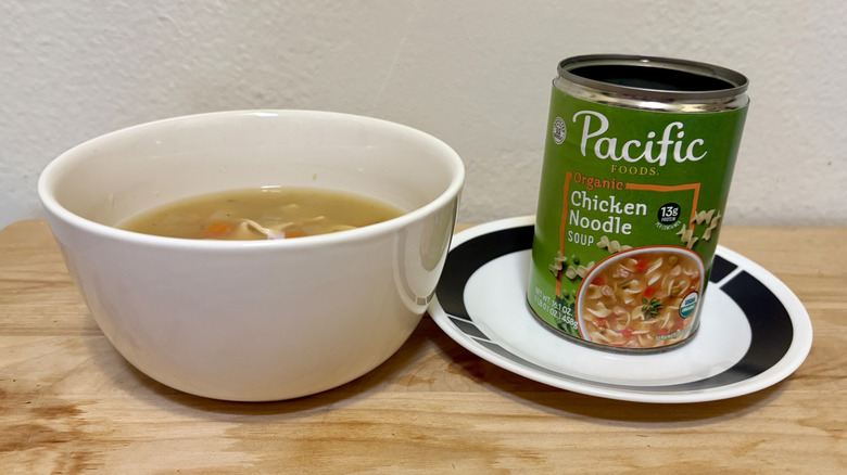 A can of Pacific Foods Organic Chicken Noodle Soup on a plate next to a prepared bowl of soup
