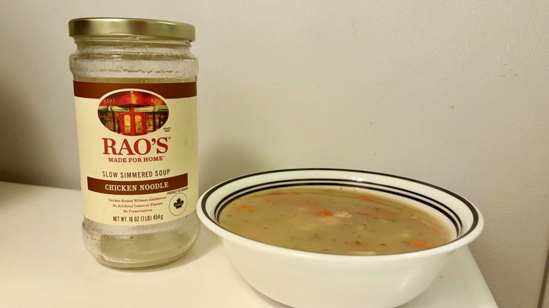 An empty jar of Rao's Chicken Noodle Soup next to a prepared bowl of soup
