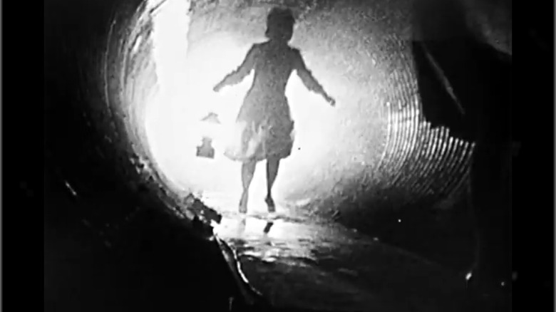 A backlit silhouette of a woman running with a lantern through a dark tunnel