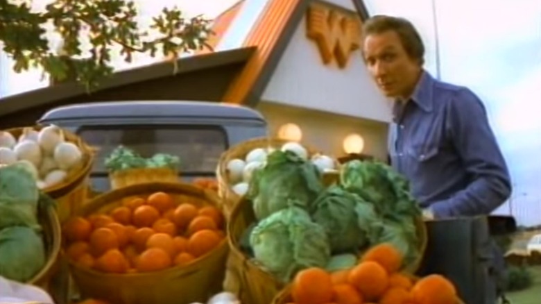 Still from commercial showing country singer Mel Tillis next to a pickup truck bed full of fresh vegetables in front of a Whataburger location