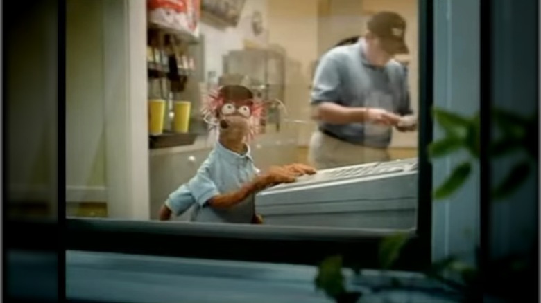 Still from a commercial showing Pepe the King Prawn in a blue polo shirt and cap working the drive-thru window