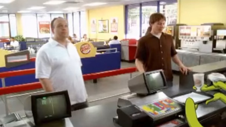 Still from commercial showing two men at a Burger King counter with animated green alien tentacles placing food on a tray in the corner