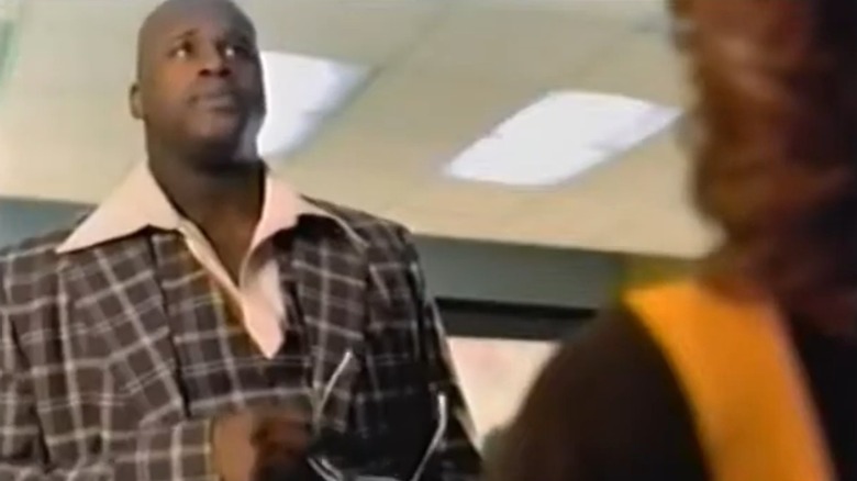 Still from commercial showing Shaquille O'Neal in a 1970s-style suit with wide collar in front of a cashier