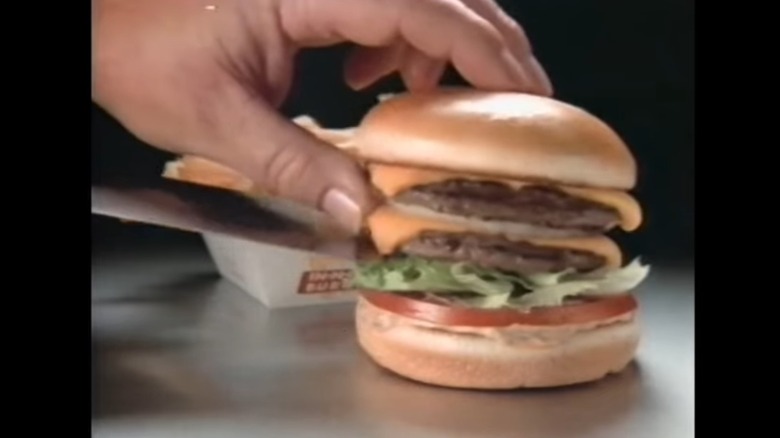 Still from a commercial showing a Double-Double with a hand holding the top bun while sliding a spatula out from under the lowest burger patty