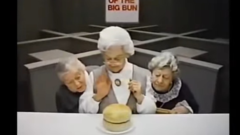 Three elderly women (Clara Peller on the right) looking down at an oversized bun on a white plate