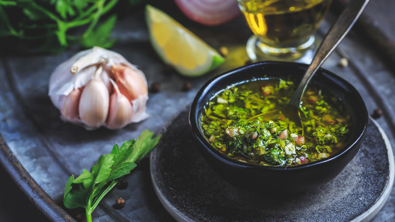 Small dish of freshly made chimichurri with a spoon, garlic, lime, and parsley