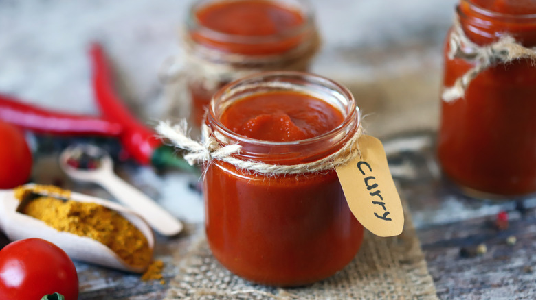 A jar of homemade curry paste with fresh ingredients surrounding it