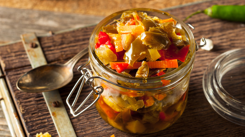 Glass jar of homemade giardiniera on a wooden board with a spoon