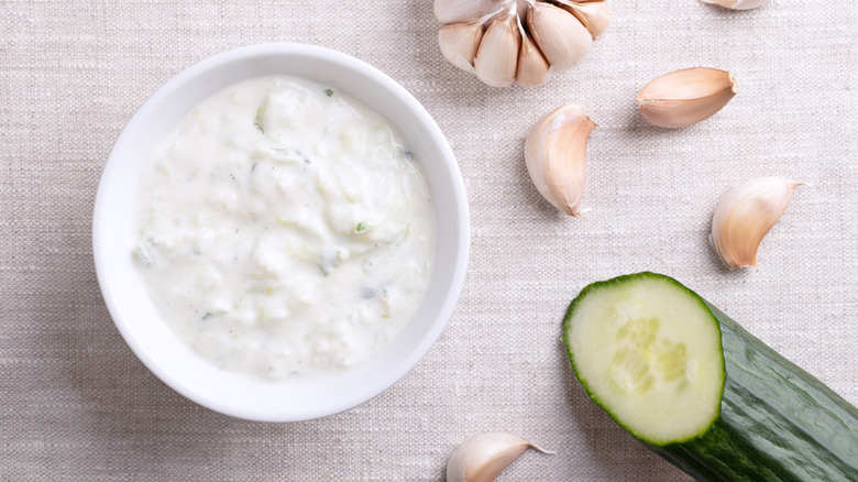Overhead view of a small bowl full of tzatziki with a cucumber and cloves of garlic