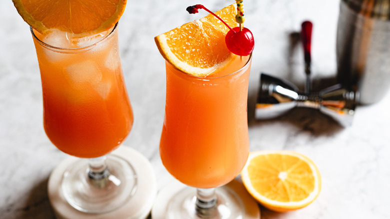 two hurricane cocktails on marble countertop with bartending tools