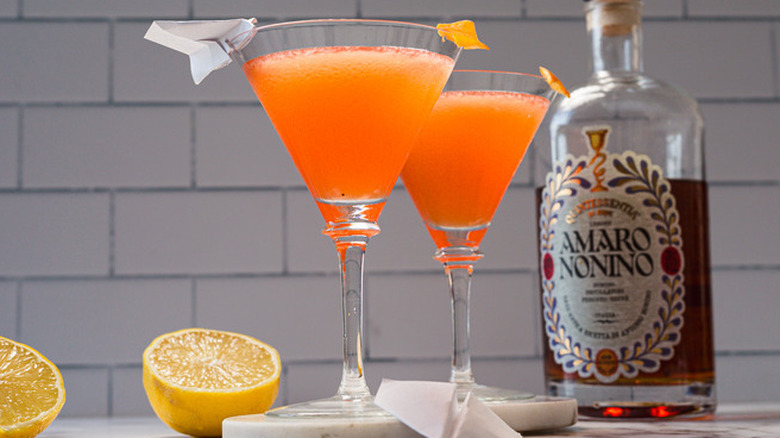 two paper plane cocktails with a halved lemons and a bottle of amaro nonino