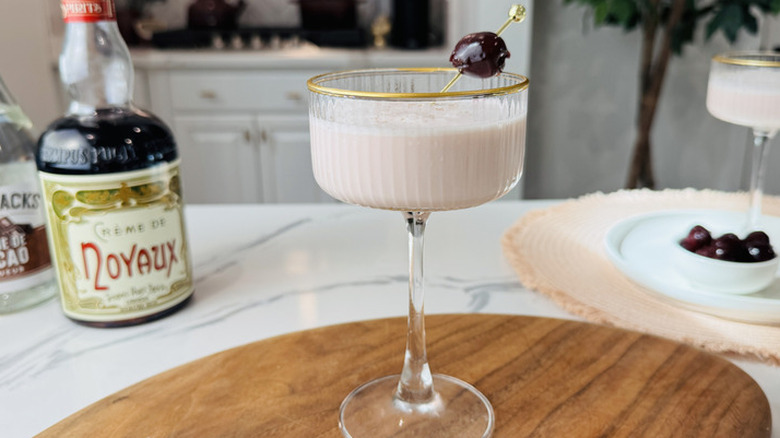 Pink squirrel cocktail on wooden cutting with various ingredients in the background