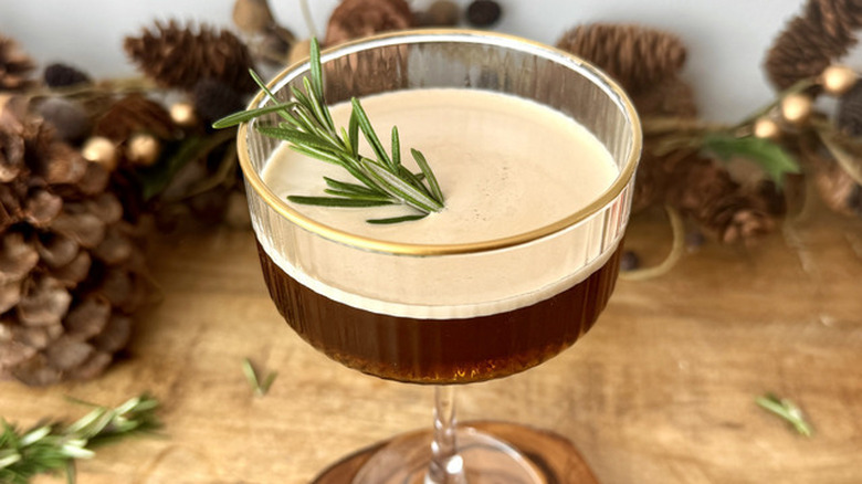 espresso martini with rosemary sprig and pine cones in the background