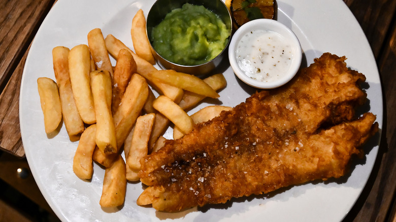 Fish and chips on a white plate with condiments