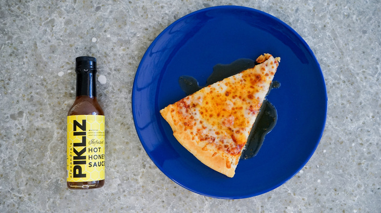 Pikliz hot honey bottle with pizza and hot honey drizzle on blue plate