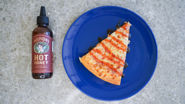 Melinda's hot honey bottle with pizza and hot honey drizzle on blue plate
