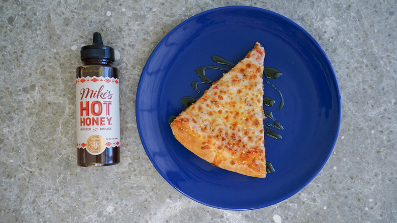 Mike's hot honey bottle with pizza and hot honey drizzle on blue plate