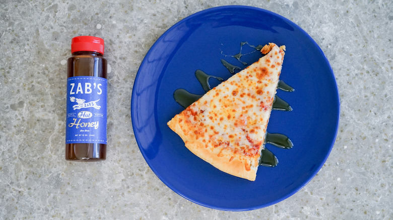 Zab's hot honey bottle with pizza and hot honey drizzle on blue plate