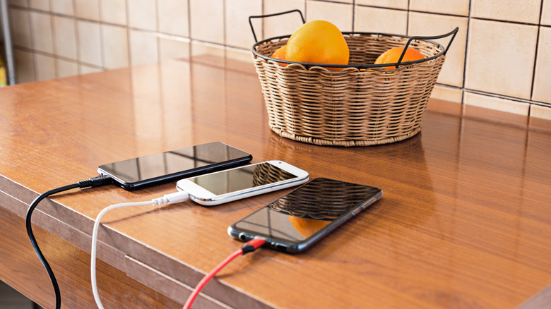 Charging three phones in kitchen with basket of oranges