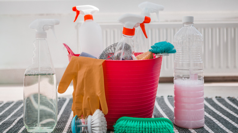 Several household cleaning products in spray bottles in a bucket