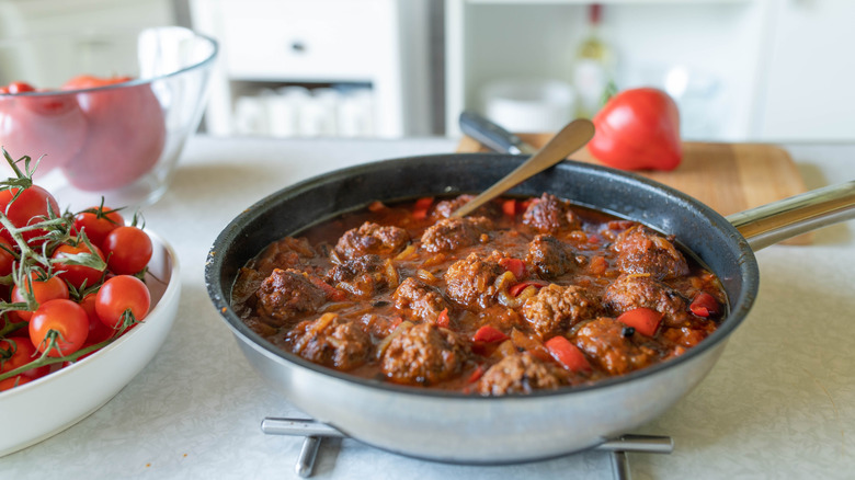 Pan of meatballs with metal trivet next to tomatoes on counter