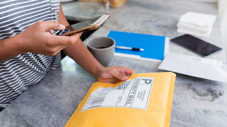 Woman looking at phone with mail and papers on kitchen counter