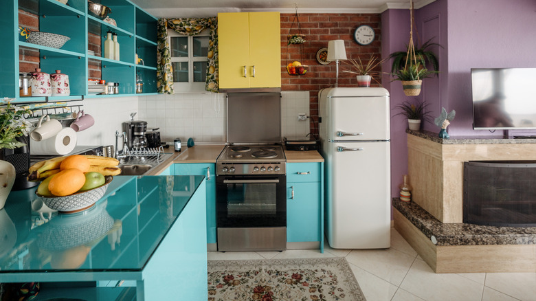 Colorful kitchen with blue counters, shelving, yellow cabinets, and a purple wall