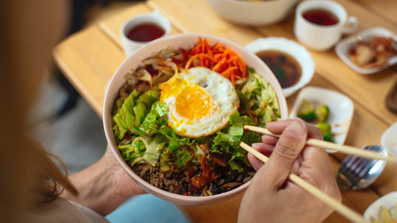 Person eating a bibimbap bowl with chopsticks