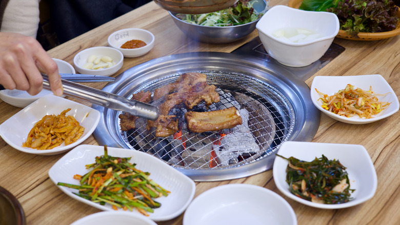 A person making samgyeopsal at Korean BBQ restaurant with various side dishes