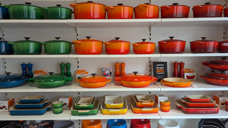 Various Le Creuset cookware organized by color on a shelf.