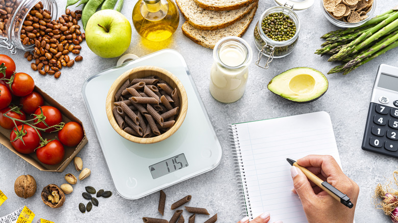 hand making notes next to kitchen scale and foodstuffs