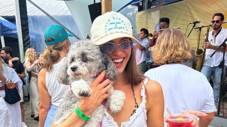 A woman holding her dog and a drink at the Cisco Beer Garden with a live band in the background