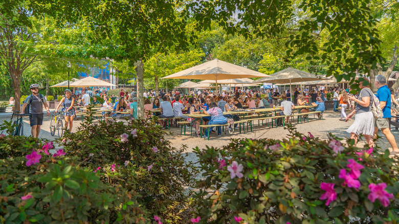 A crowded beer garden on a summer day with flowering bushes