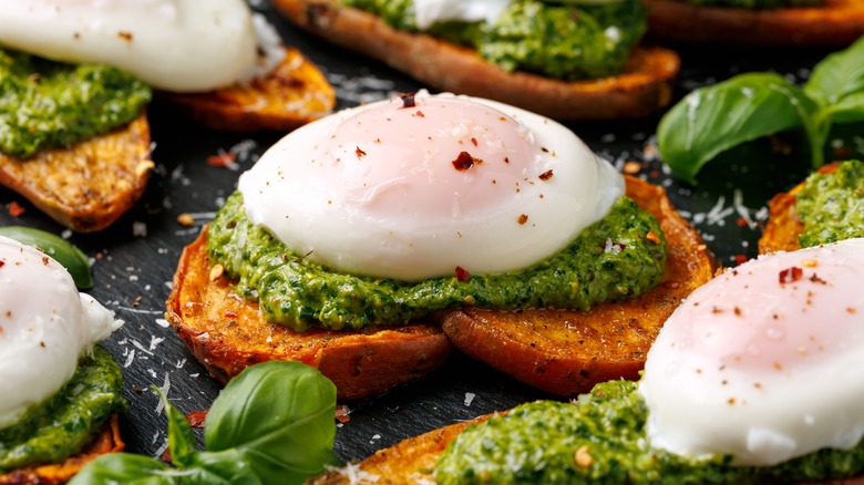 A fried egg on top of pesto that is spread onto two pieces of toast