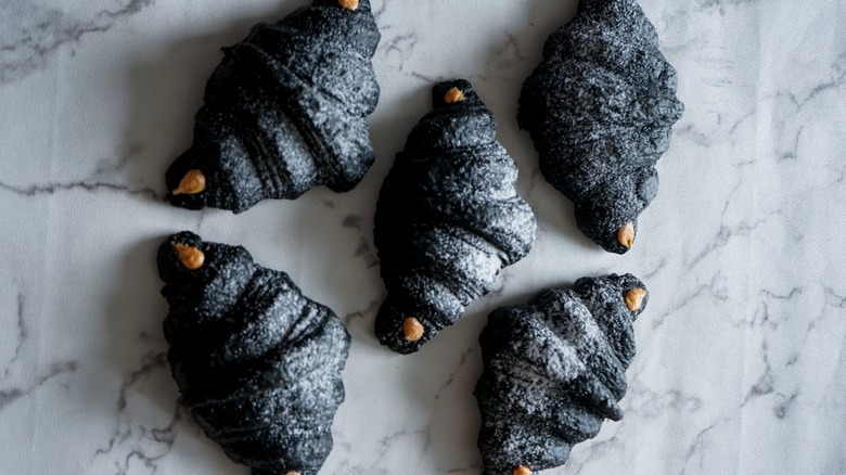 Five black charcoal croissants on a marble countertop